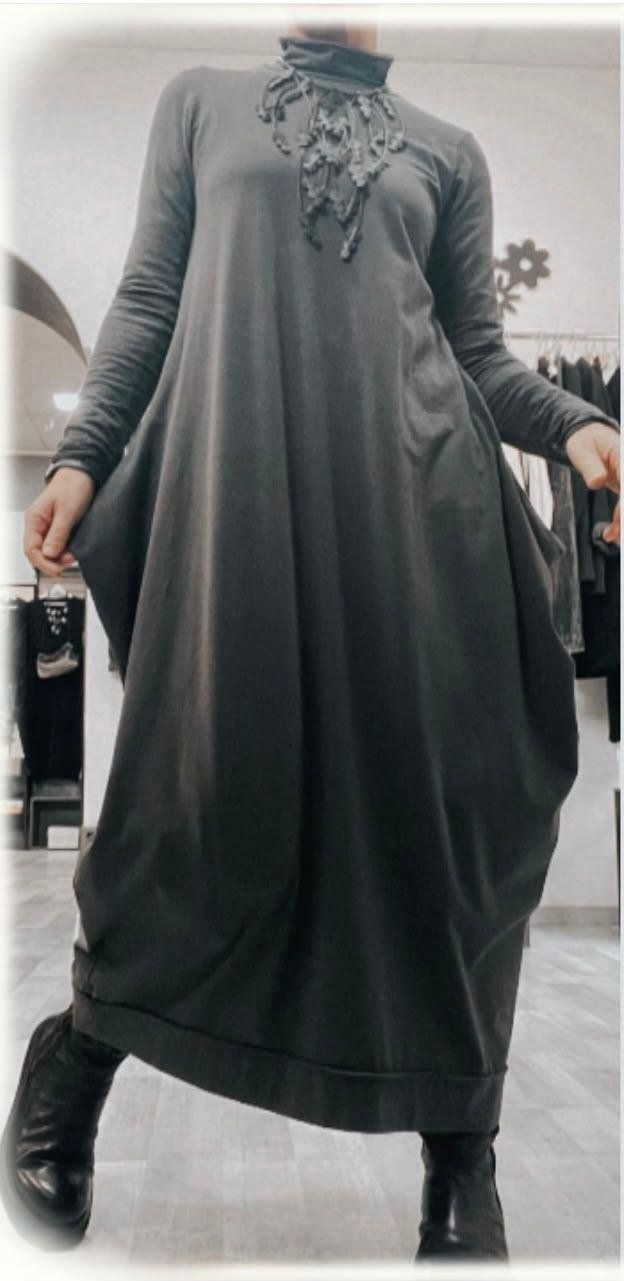 Abito lungo grigio dalla linea a bolla, con collo alto e dettaglio decorato sul davanti, indossato con anfibi neri.