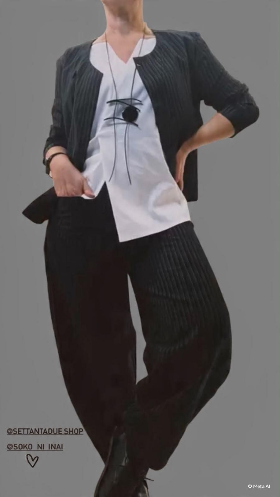 Giacca nera a righe sottili sopra una tunica bianca asimmetrica, pantaloni neri ampi e collana con pendente tondo.