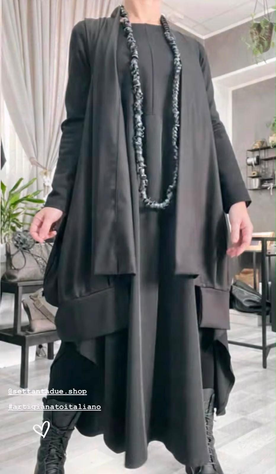 Cardigan lungo nero aperto sopra un abito nero, collana lunga di elementi in pelle e anfibi stringati.