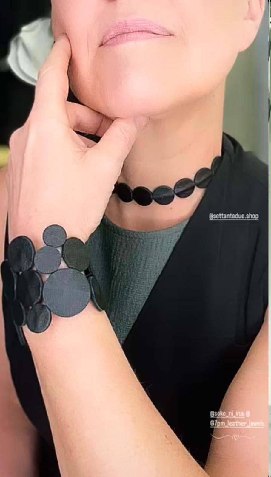Girocollo e bracciale artigianali composti da dischi di pelle nera, indossati su un abito scuro.