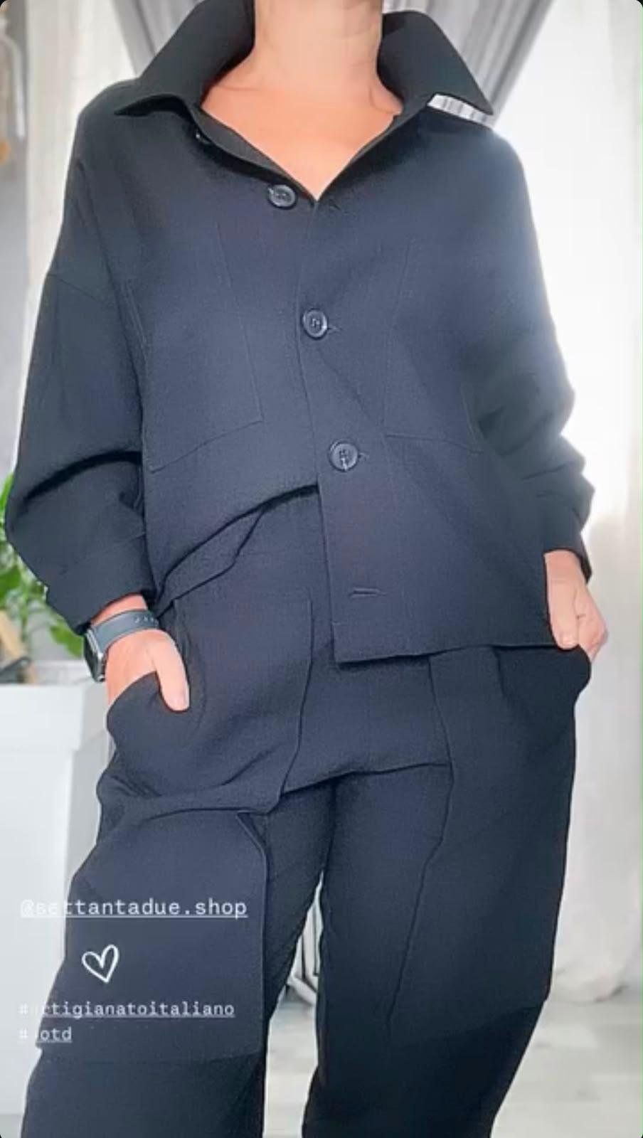 Completo nero: camicia-giacca con colletto ampio e bottoni tono su tono, abbinata a un pantalone morbido.